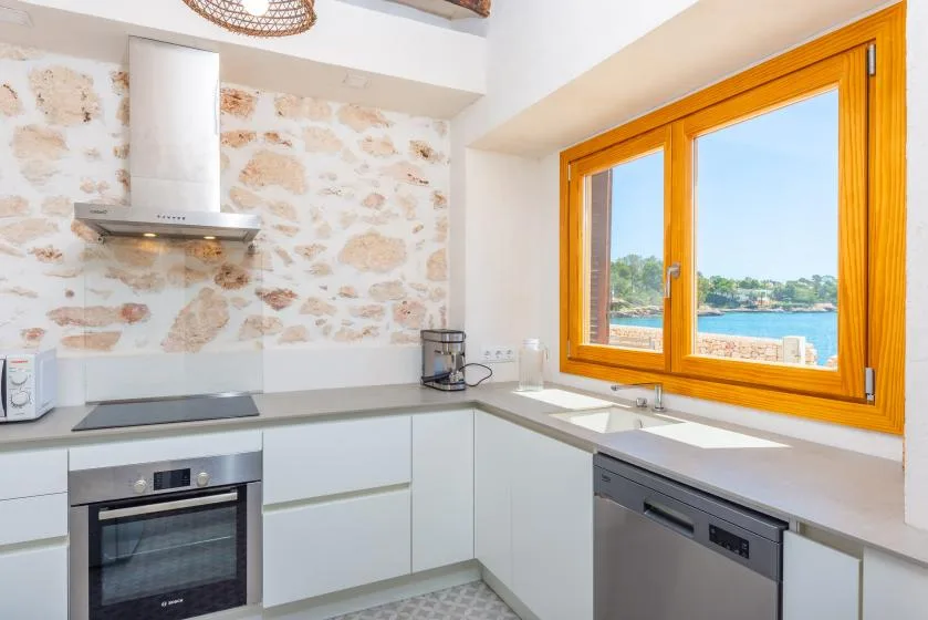 Una cocina luminosa con gabinetes blancos y una gran ventana con vista al agua.