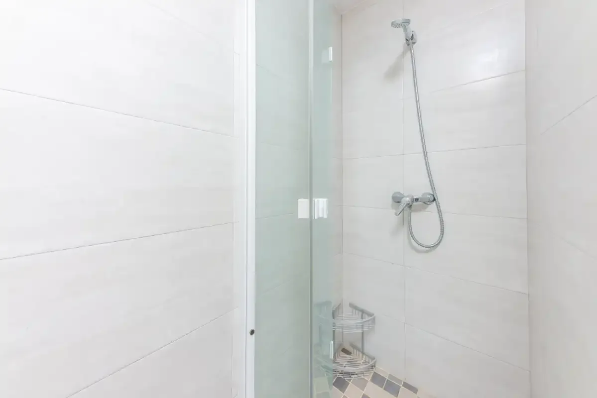 Una ducha de baño con azulejos, alcachofa de mano y controles en la pared.