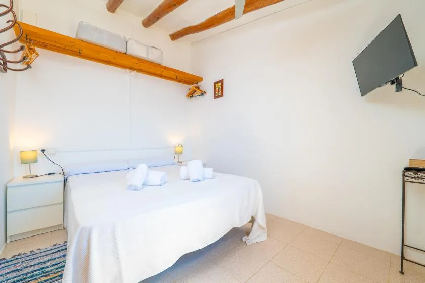Un dormitorio luminoso con una cama blanca y vigas de madera expuestas en el techo.