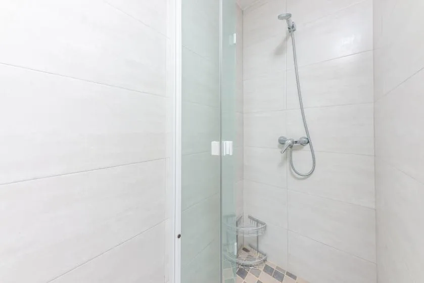 Una ducha con azulejos, panel de vidrio y ducha de mano.