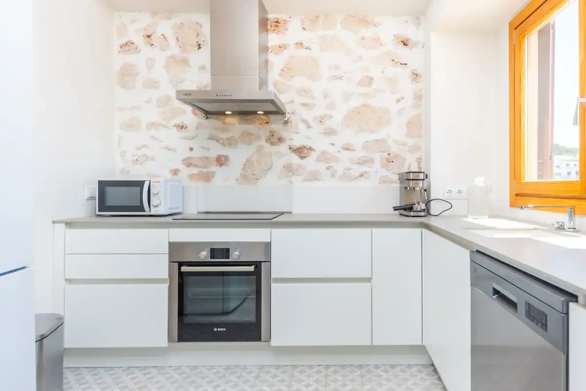 Una cocina luminosa con armarios blancos y un salpicadero de aspecto pétreo.