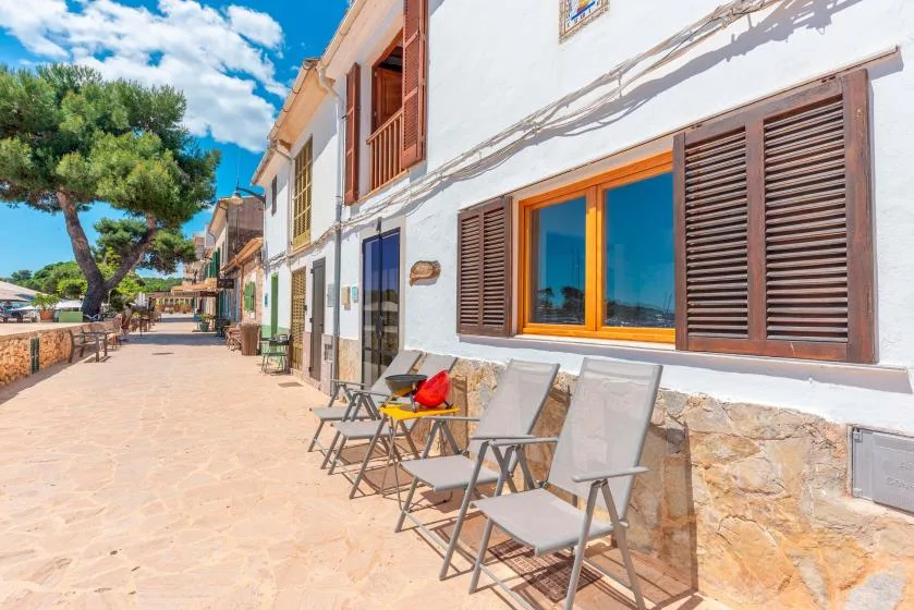 Un paseo exterior soleado junto a un edificio blanco, con sillas plegables junto a la pared.