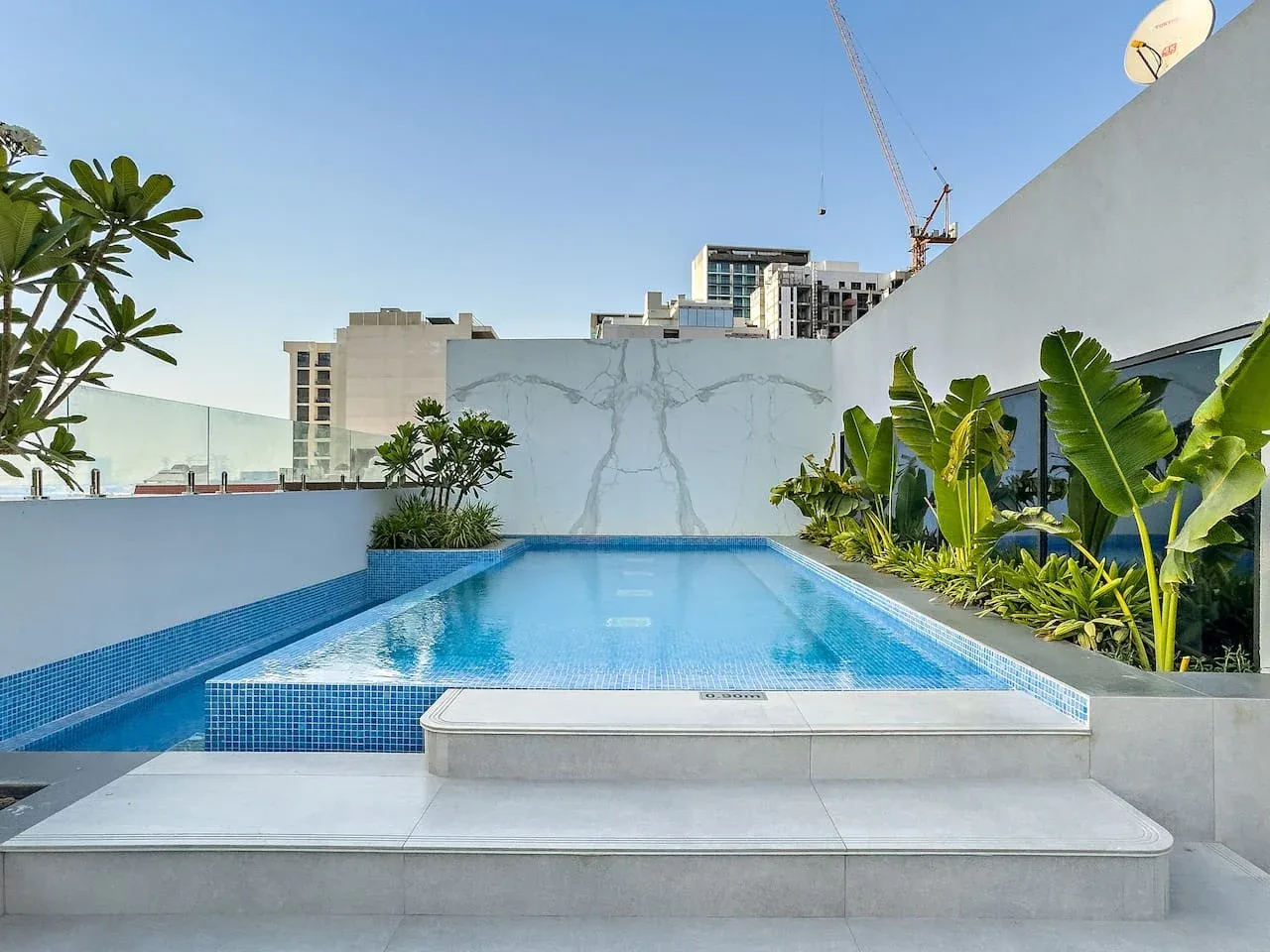 Una piscina al aire libre está rodeada de superficies con azulejos y plantas tropicales.