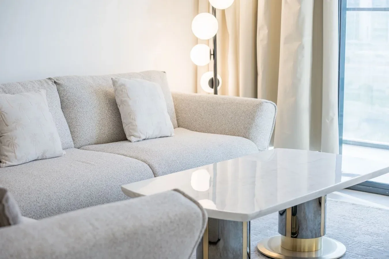 Una sala luminosa con asientos claros, una mesa de centro y una lámpara de pie.