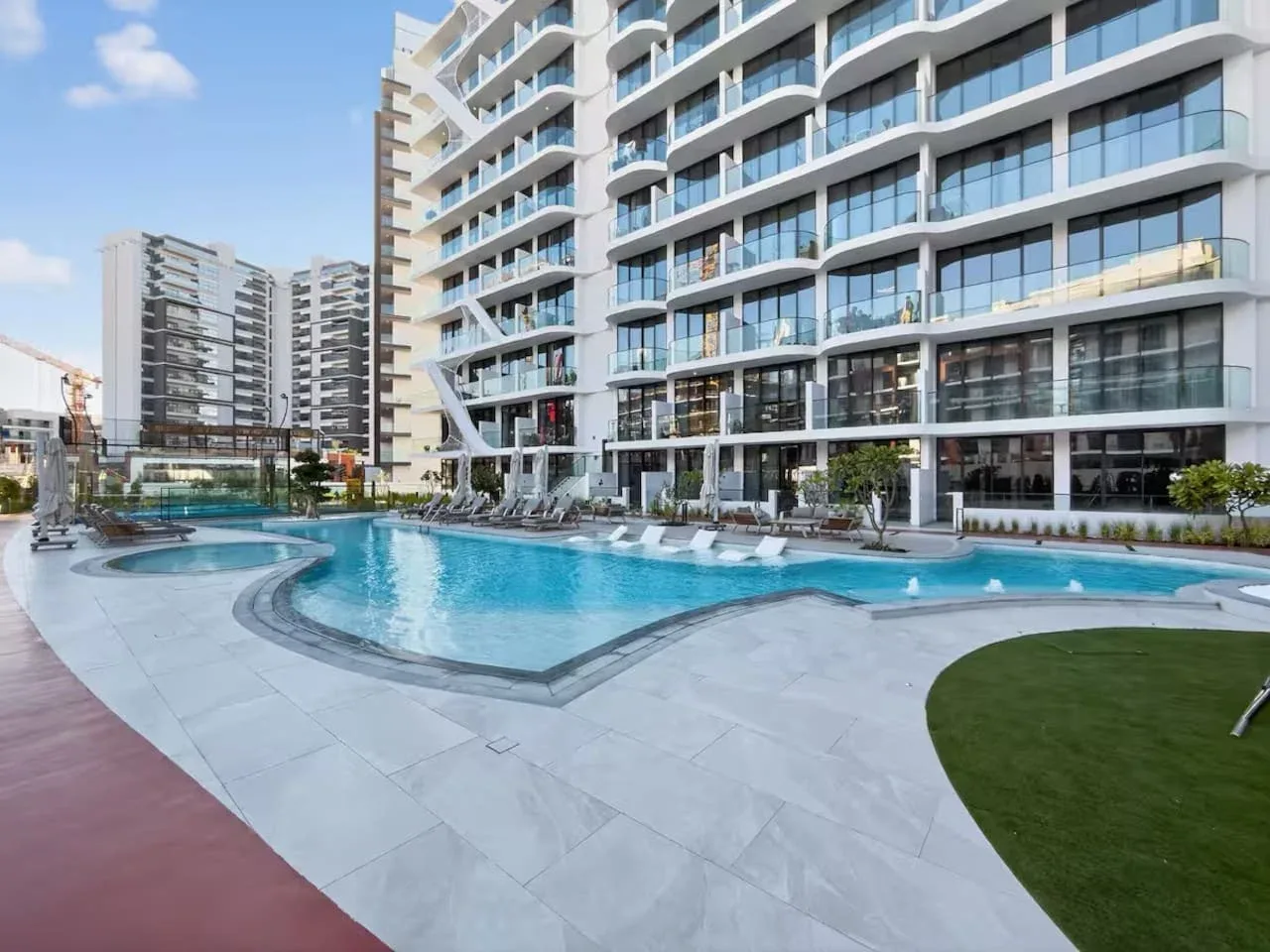 Una piscina y asientos de descanso están junto a un edificio moderno de varios pisos.