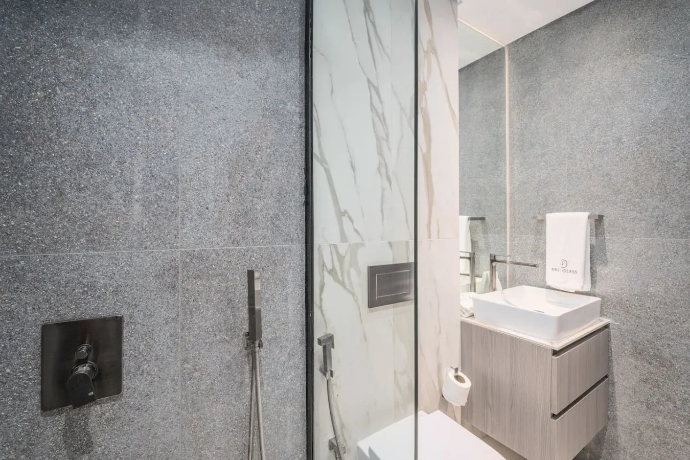 Un baño moderno con ducha, lavabo y paredes de azulejos grises.