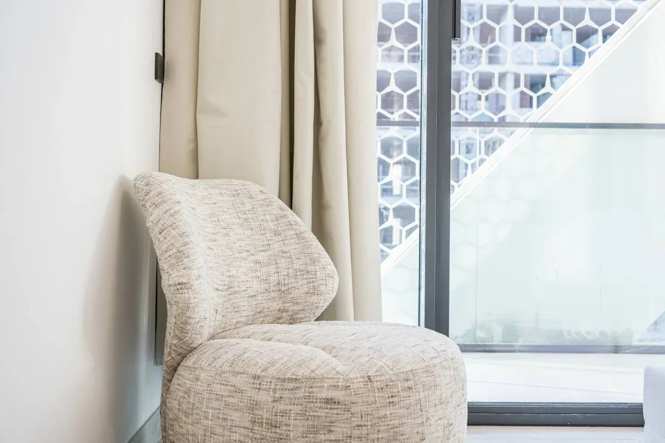 Un asiento acolchado está junto a una ventana con cortinas y una barandilla de vidrio.