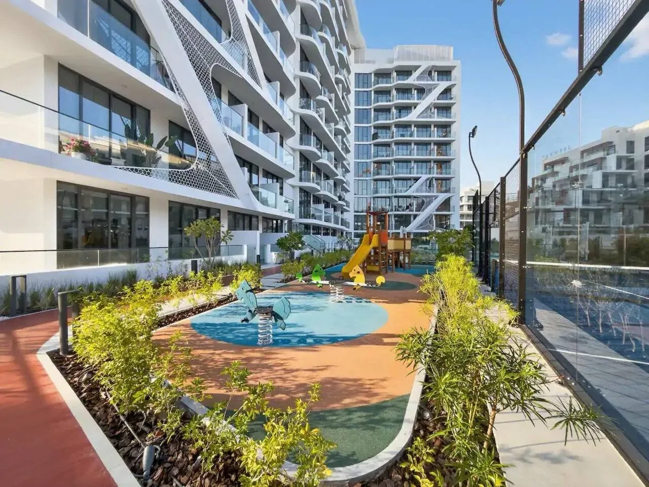 Un parque infantil al aire libre se encuentra entre edificios modernos, con toboganes y una zona de juegos acuáticos.