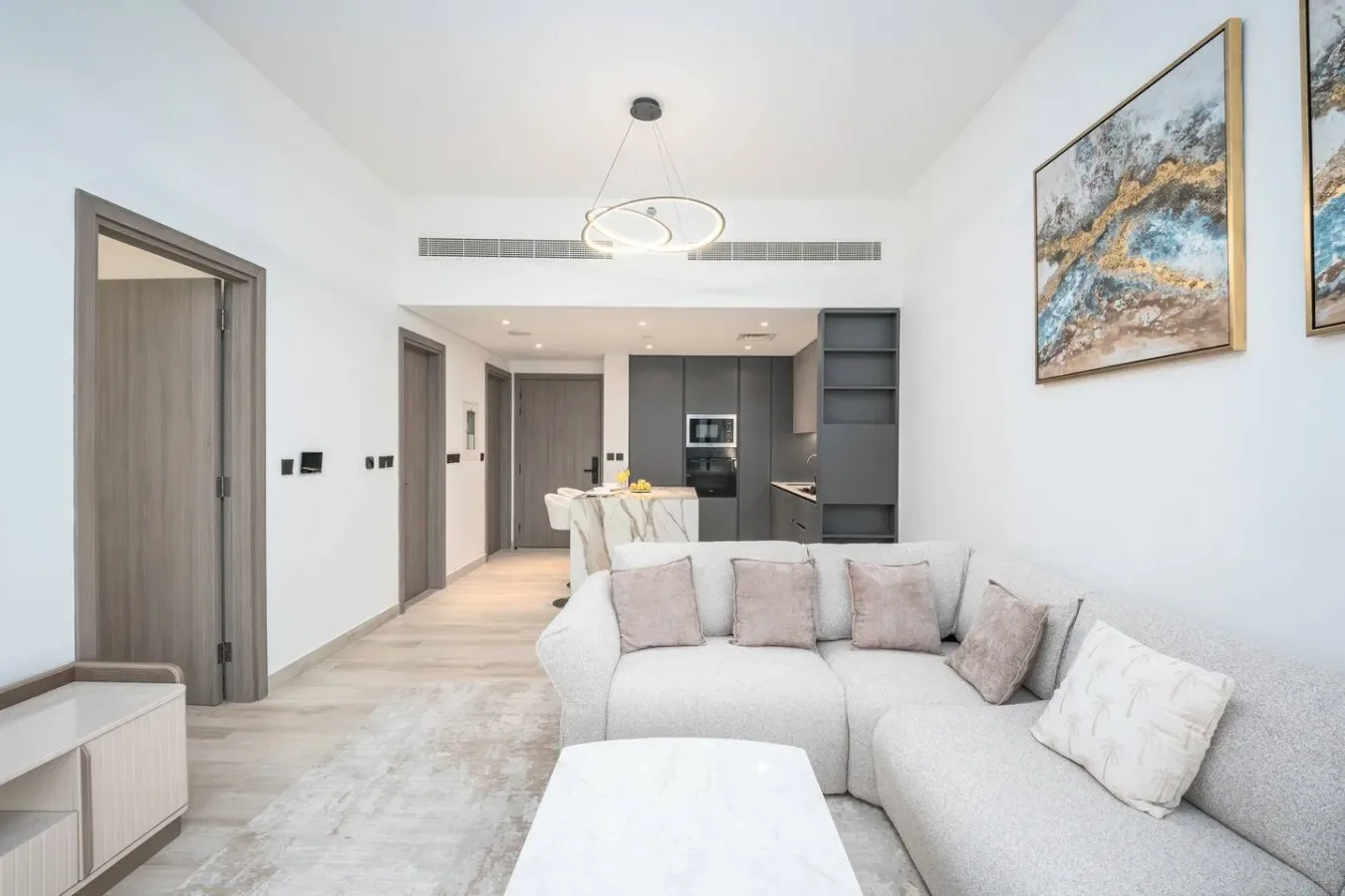 Una sala luminosa con un sofá seccional y una cocina abierta al fondo.
