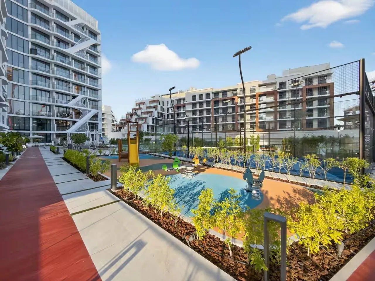 Un patio al aire libre con senderos ajardinados y una pequeña zona de juegos azul entre edificios de apartamentos.