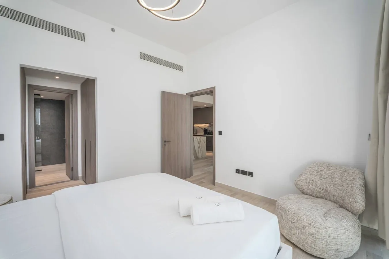 Un dormitorio luminoso con una cama y una silla tapizada de formas redondeadas.