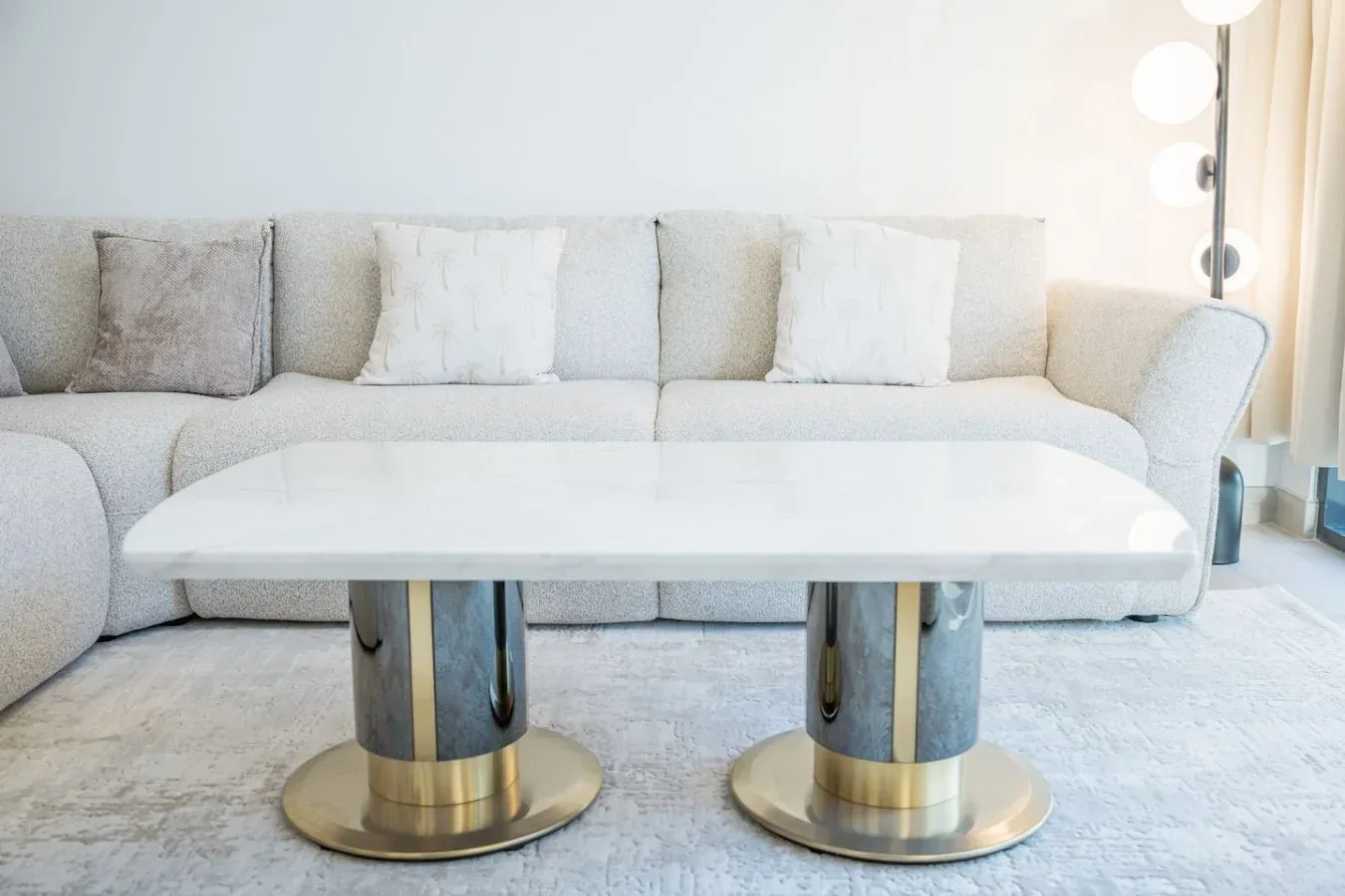Una sala luminosa con un sofá seccional claro y una mesa blanca baja.