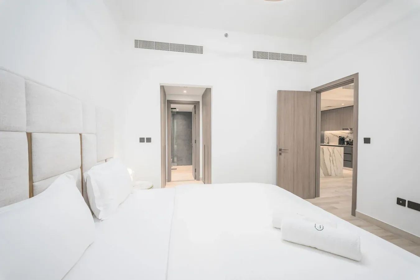 Un dormitorio luminoso con ropa de cama blanca y una puerta abierta al espacio contiguo.