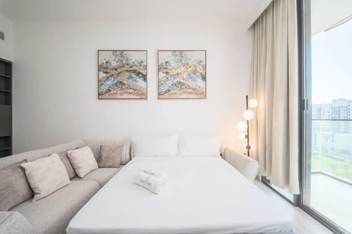 Un dormitorio luminoso con una cama grande, asientos grises y una lámpara de pie junto a la ventana.
