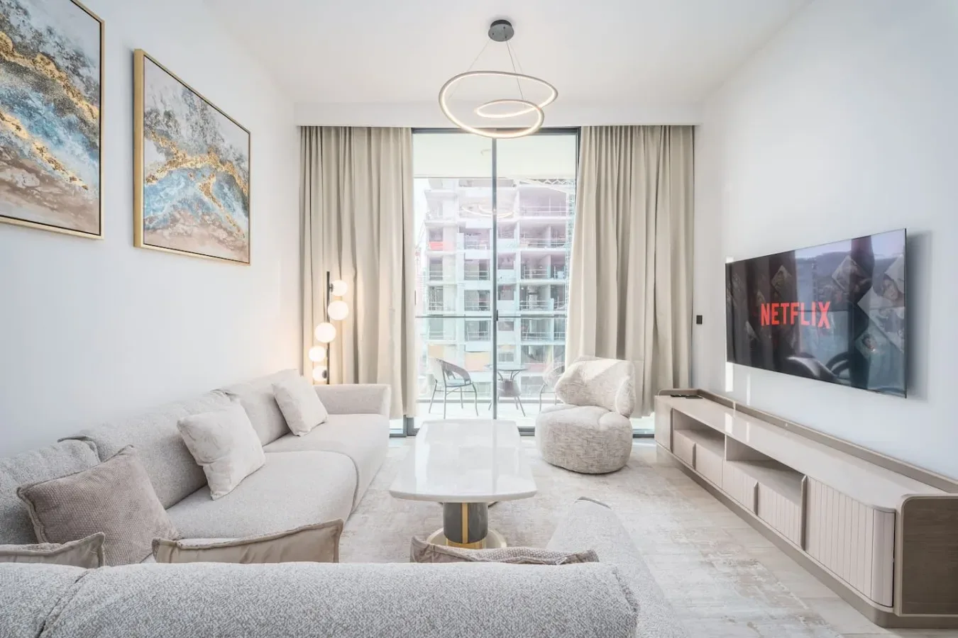 Una sala luminosa tiene asientos claros, una mesa de centro y un televisor.