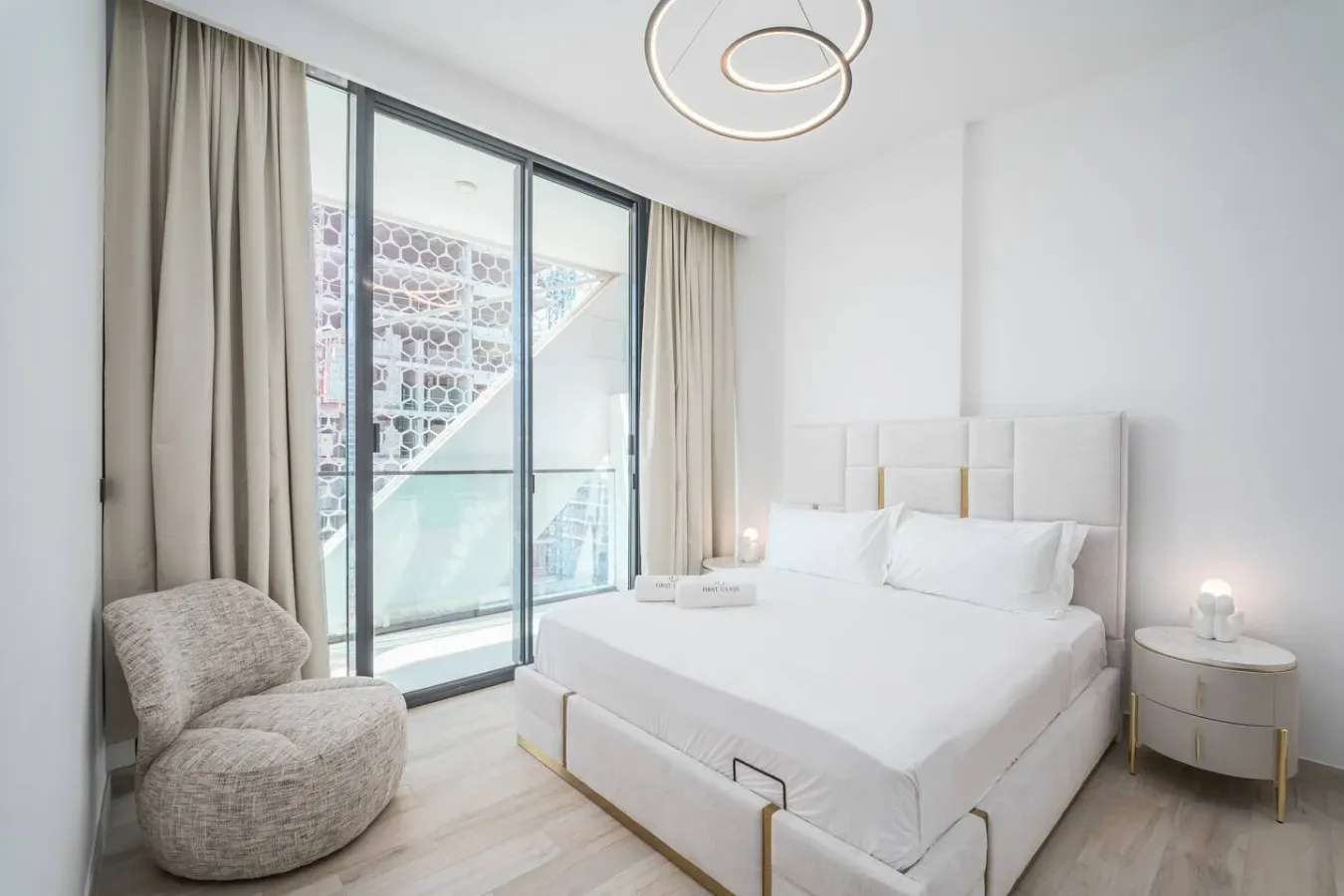 Un dormitorio luminoso con una cama blanca junto a grandes puertas de cristal y cortinas.