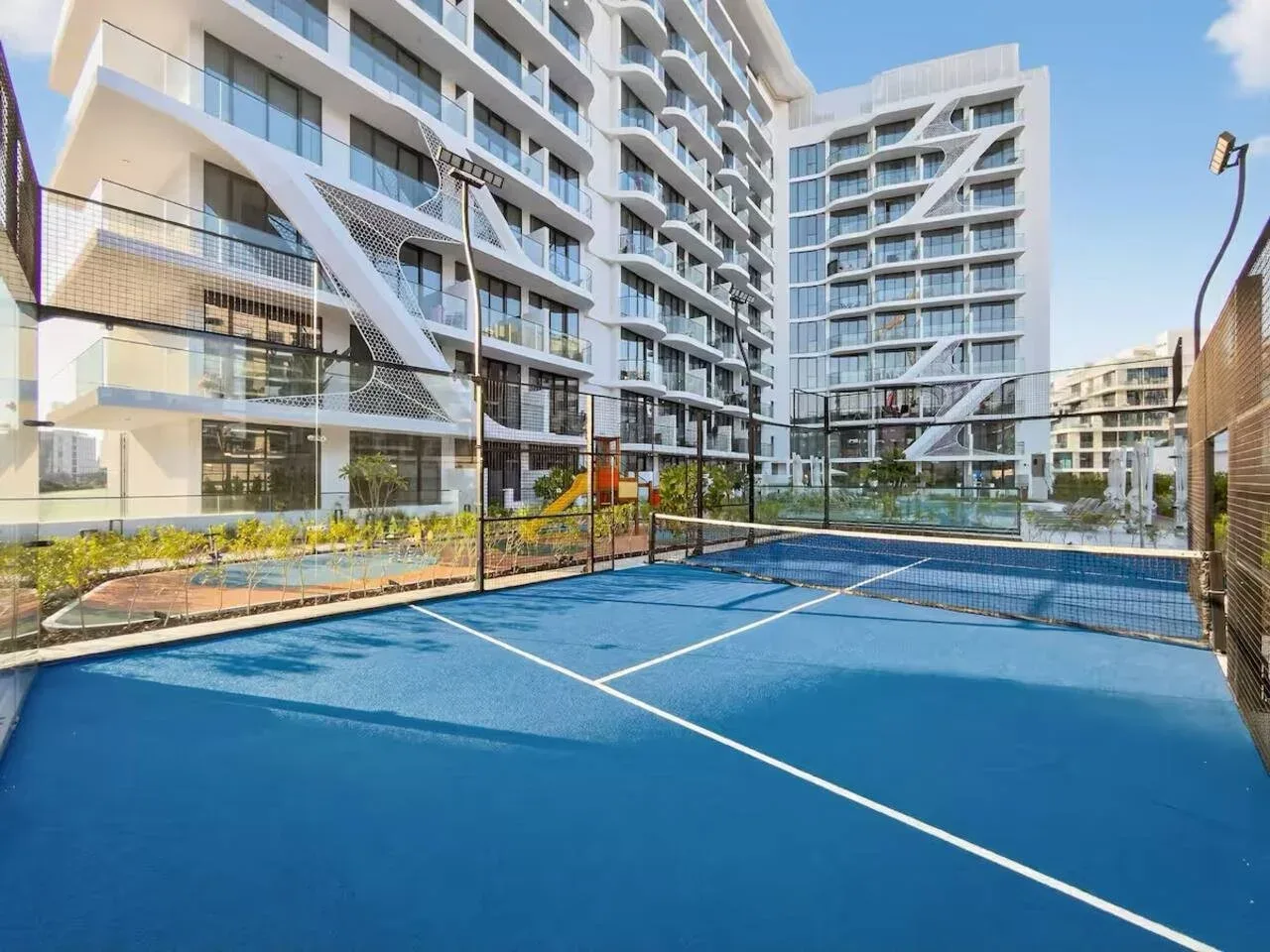 Una pista de tenis azul está junto a edificios de apartamentos modernos y jardines.