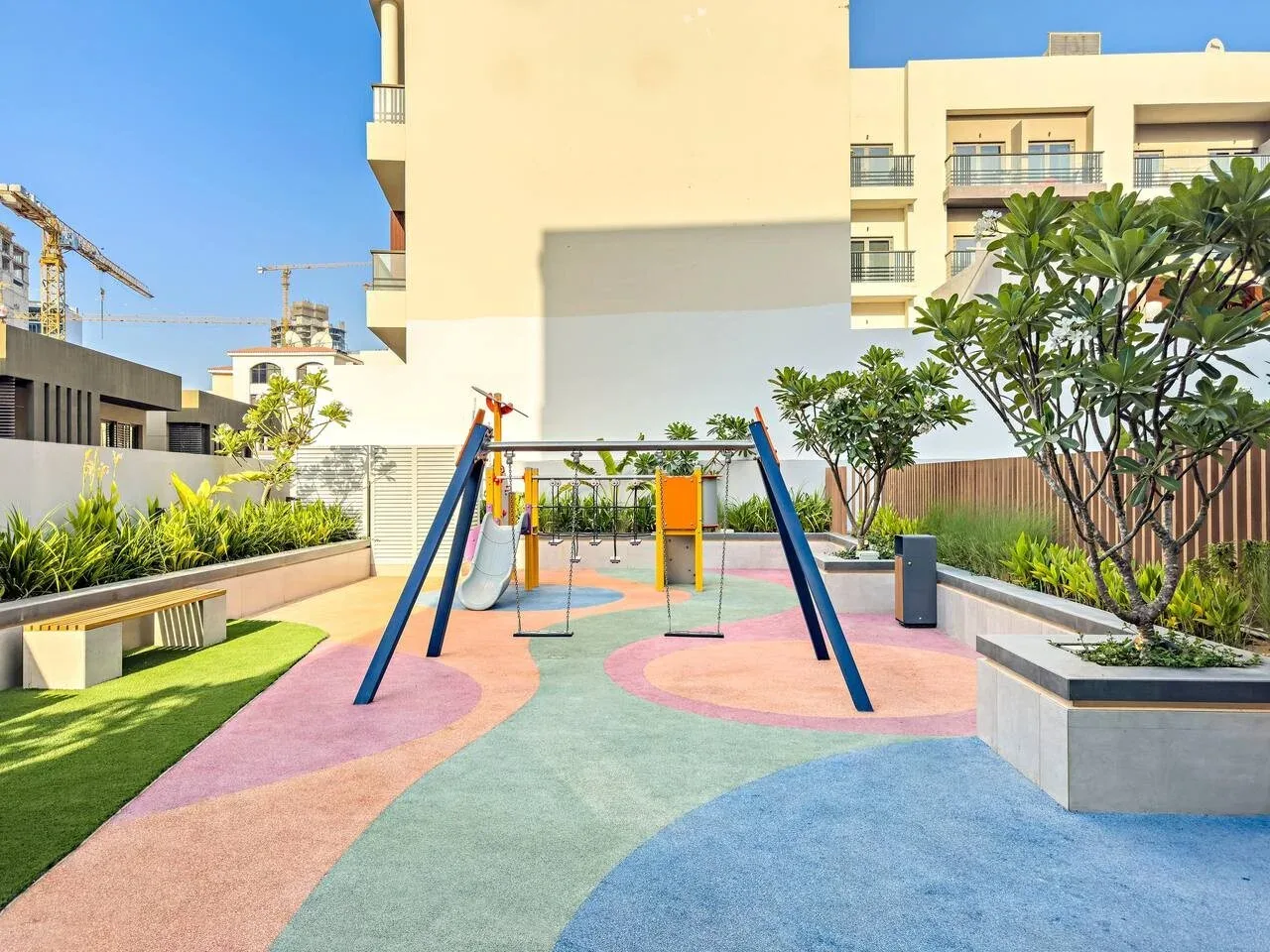 Un parque infantil al aire libre tiene columpios, un tobogán y jardineras.