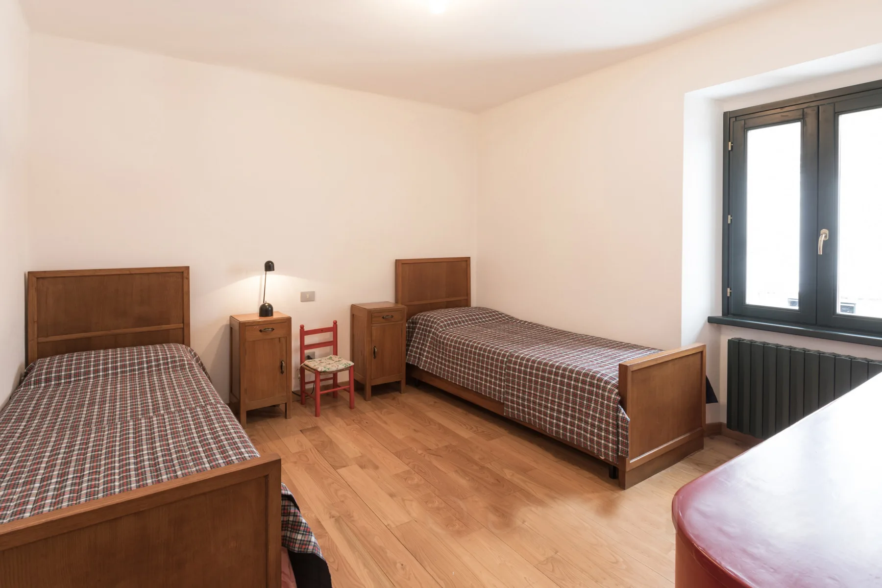 A bedroom with two beds, bedside furniture, and a large window.