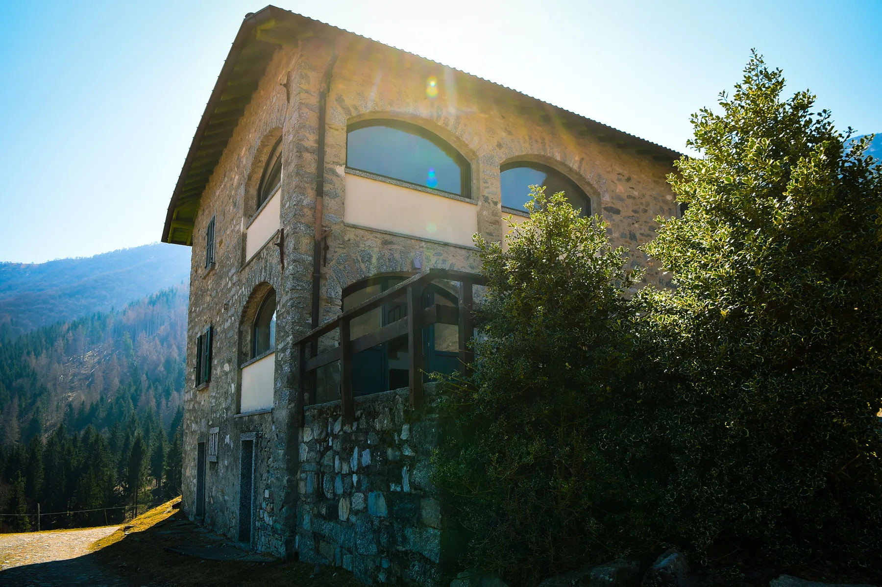 A stone building stands among trees with a forested hillside behind it.