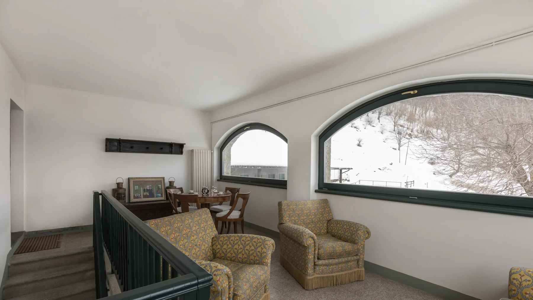 A lounge with patterned seating beside large arched windows.