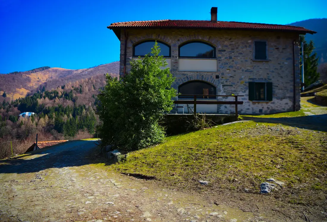 A stone house stands beside a grassy slope, with hills in the background.