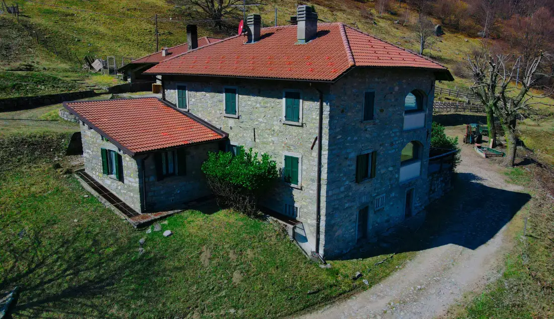A stone house with red tiled roofs sits beside a gravel drive.