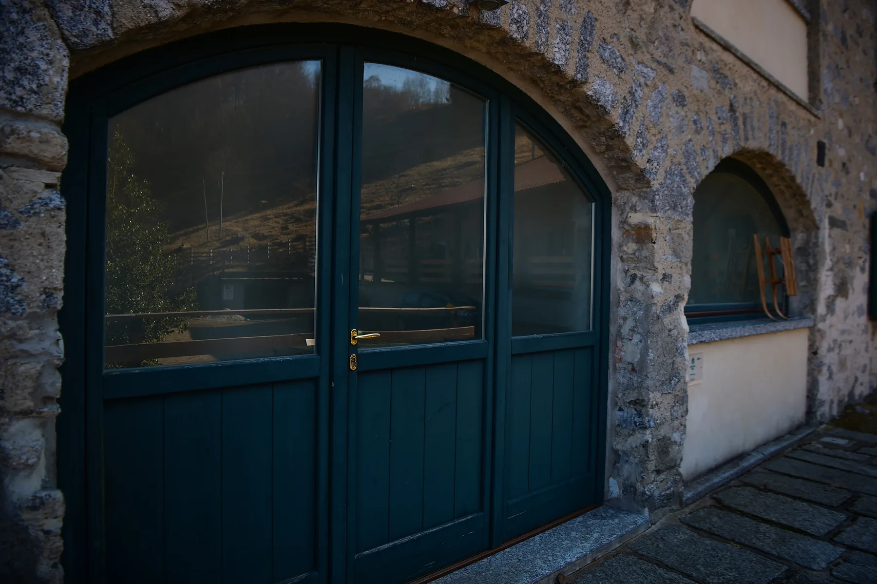 Dark teal doors and a window are set into a stone exterior wall.