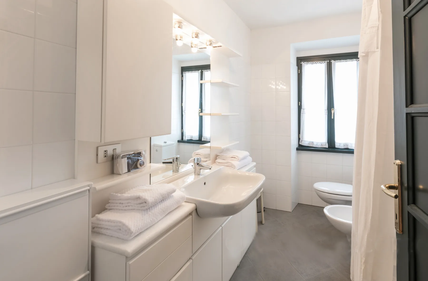 A bright bathroom has a sink, folded towels, and windows.