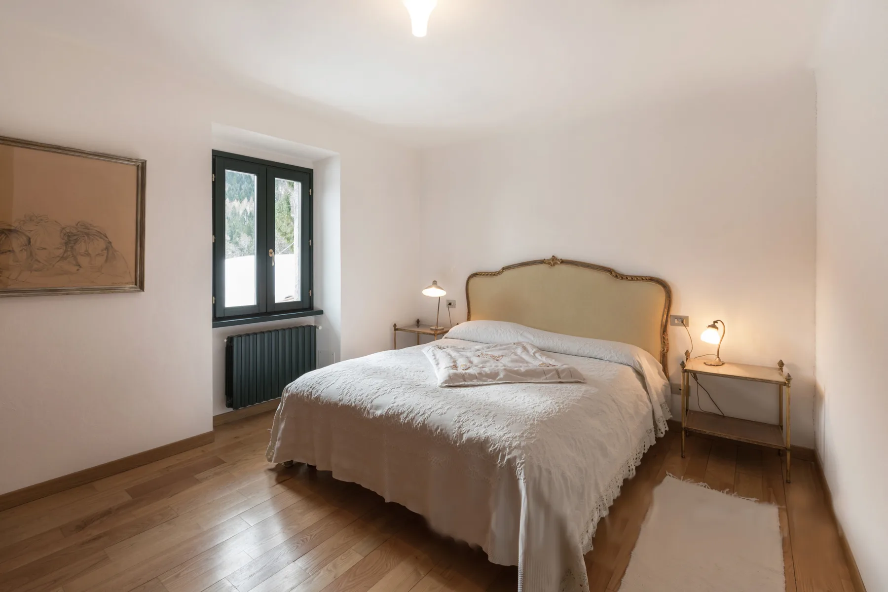 A bedroom with a bed, bedside tables, and a window.