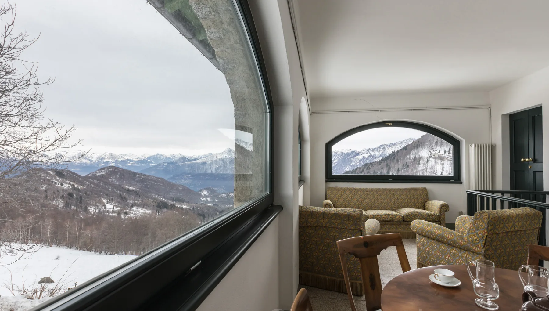 A sitting room with seating beside large windows overlooking snowy mountains.