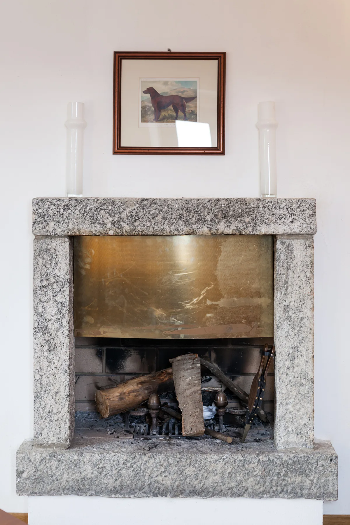A stone fireplace with logs in the hearth and a framed picture above.