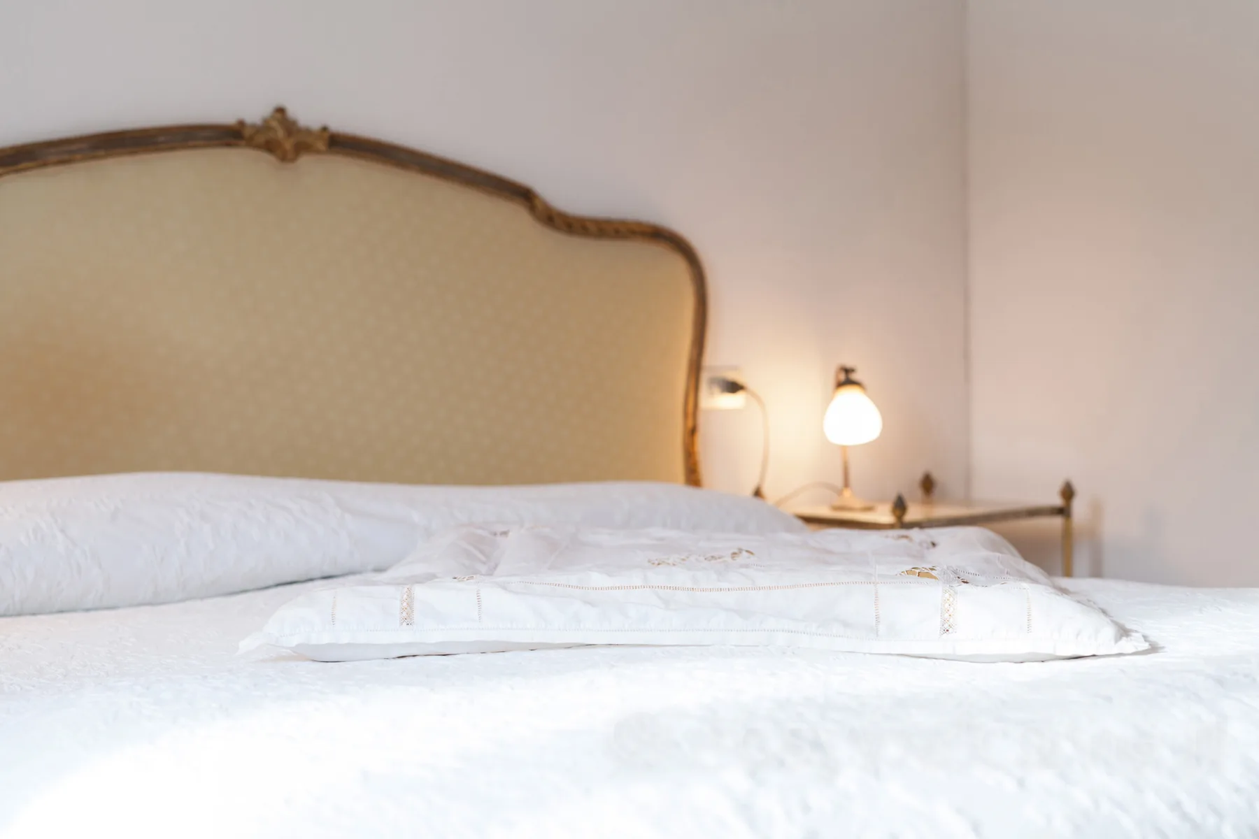 A bedroom with white bedding and a curved upholstered headboard.