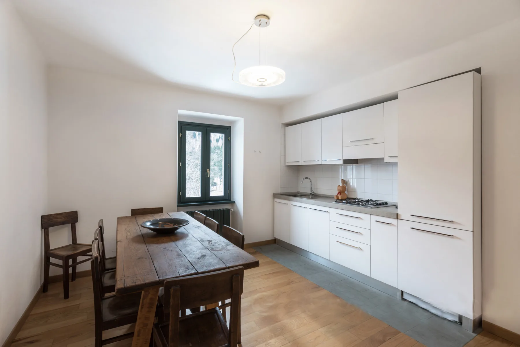A dining area beside a white kitchen, with a wooden table and chairs.