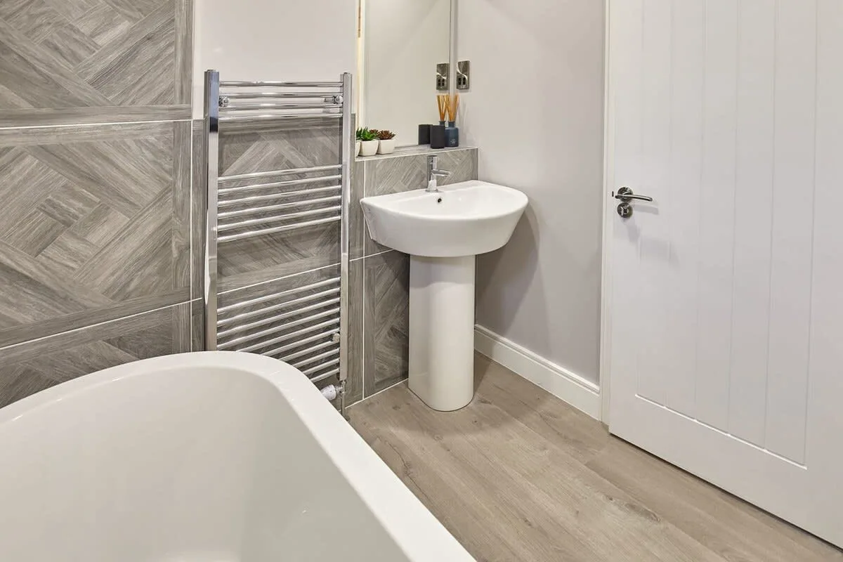 A bathroom with a freestanding bathtub, pedestal sink, and heated towel rail.