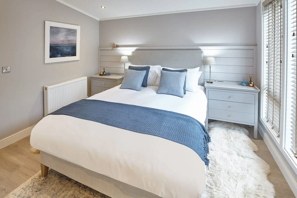 A bedroom with a neatly made bed, blue cushions, and bedside cabinets.