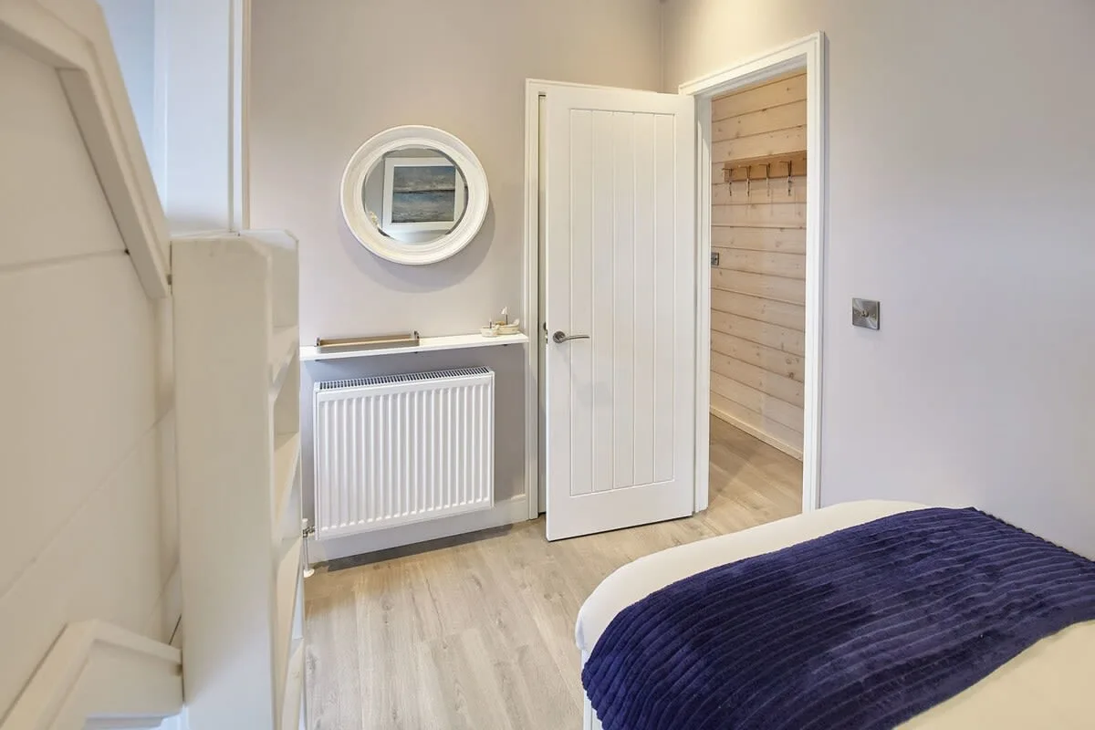 A bedroom with a bed, radiator, and an open doorway to a wood-paneled area.