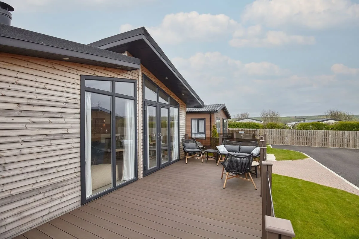 A wooden deck beside a modern house overlooks a lawn and paved path.