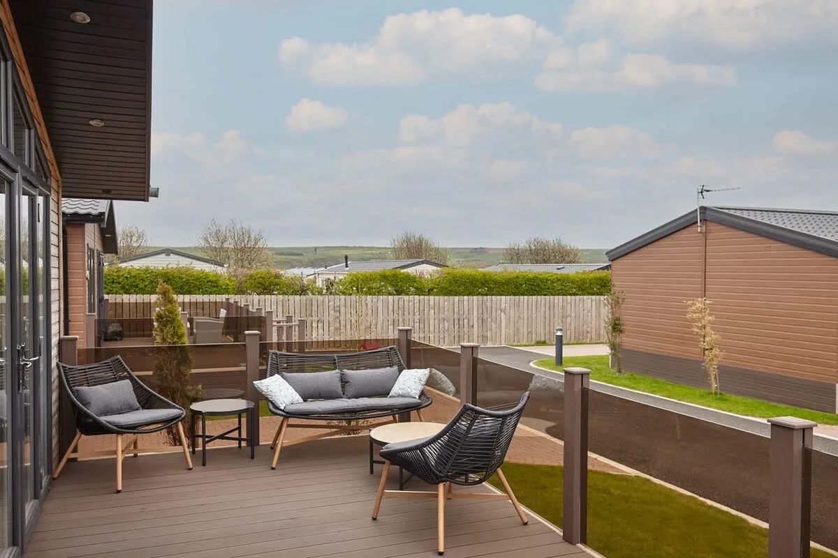 A wooden deck with outdoor seating overlooks a fenced lawn and nearby buildings.