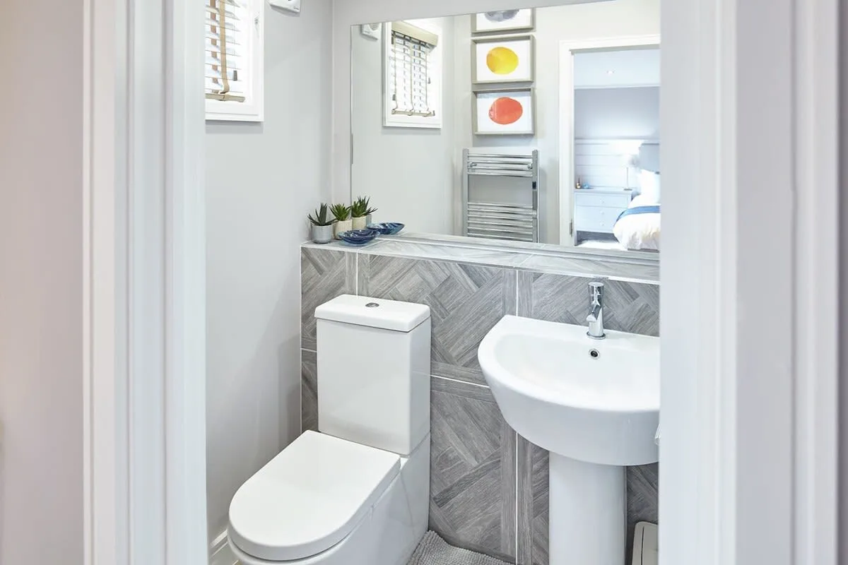A bathroom with a toilet, pedestal sink, and gray patterned wall tiles.