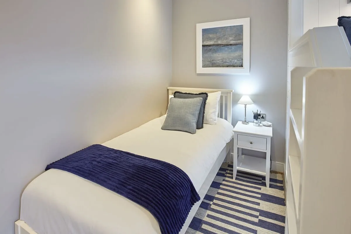 A single bed with white bedding and a dark blue throw sits beside a small bedside table.