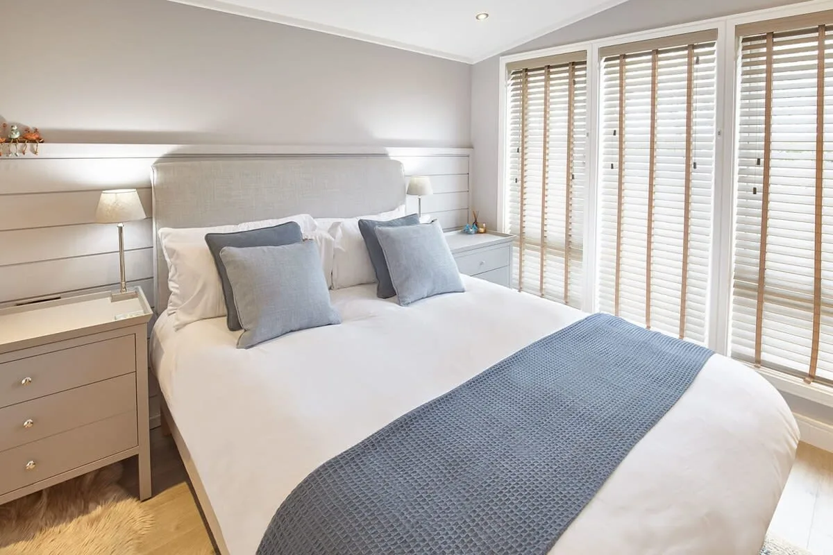 A bright bedroom with a neatly made bed and wooden window blinds.