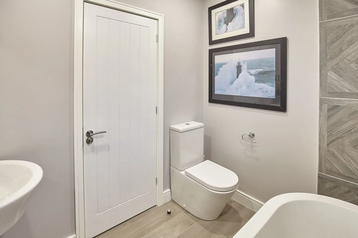 A bathroom with a toilet, framed pictures, and a partial bathtub.