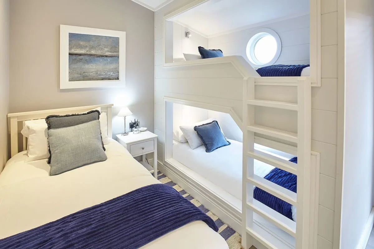 A bright bedroom with white bunk beds, blue bedding, and a framed landscape picture.