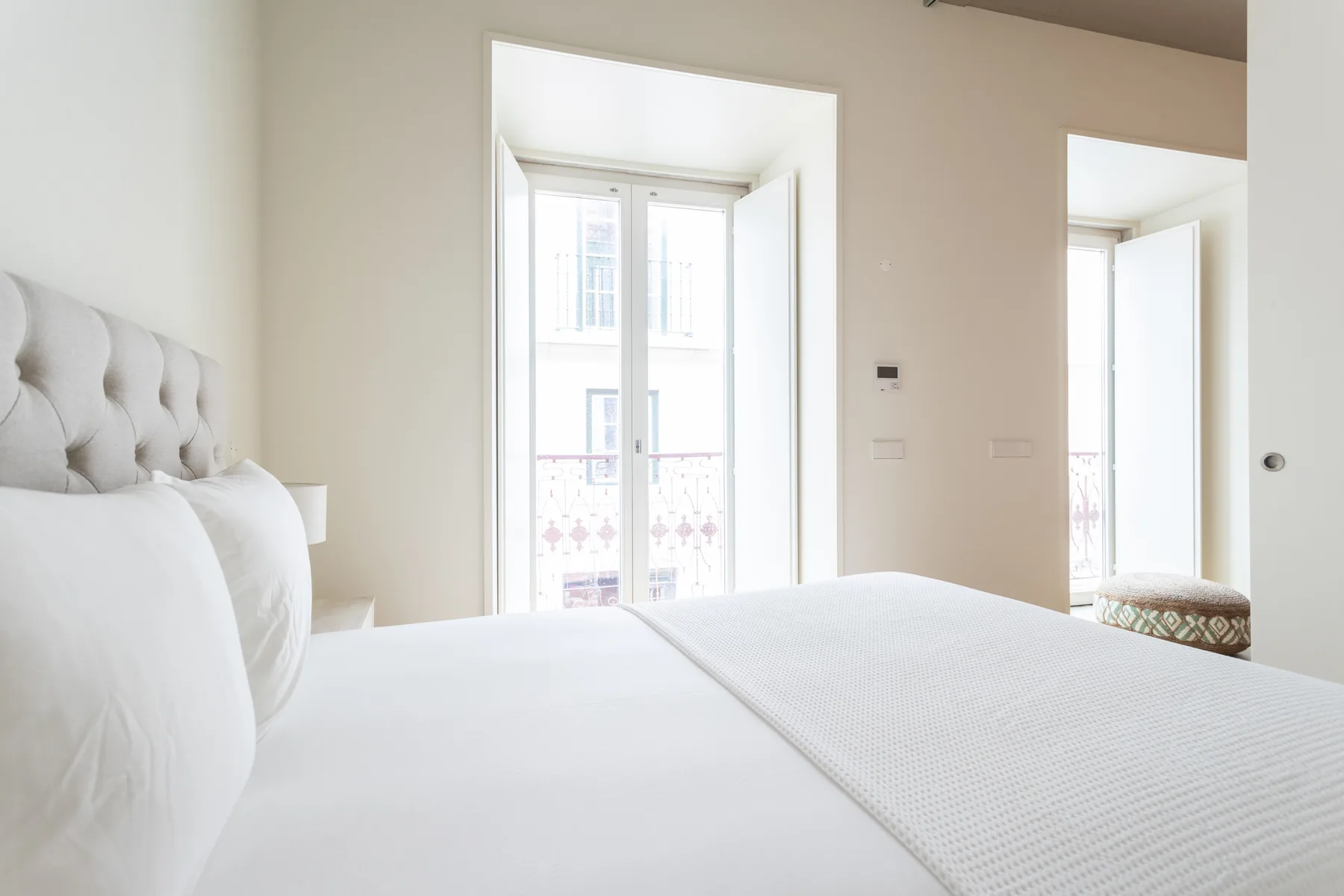 Un dormitorio luminoso con una cama bien hecha y ventanas altas.