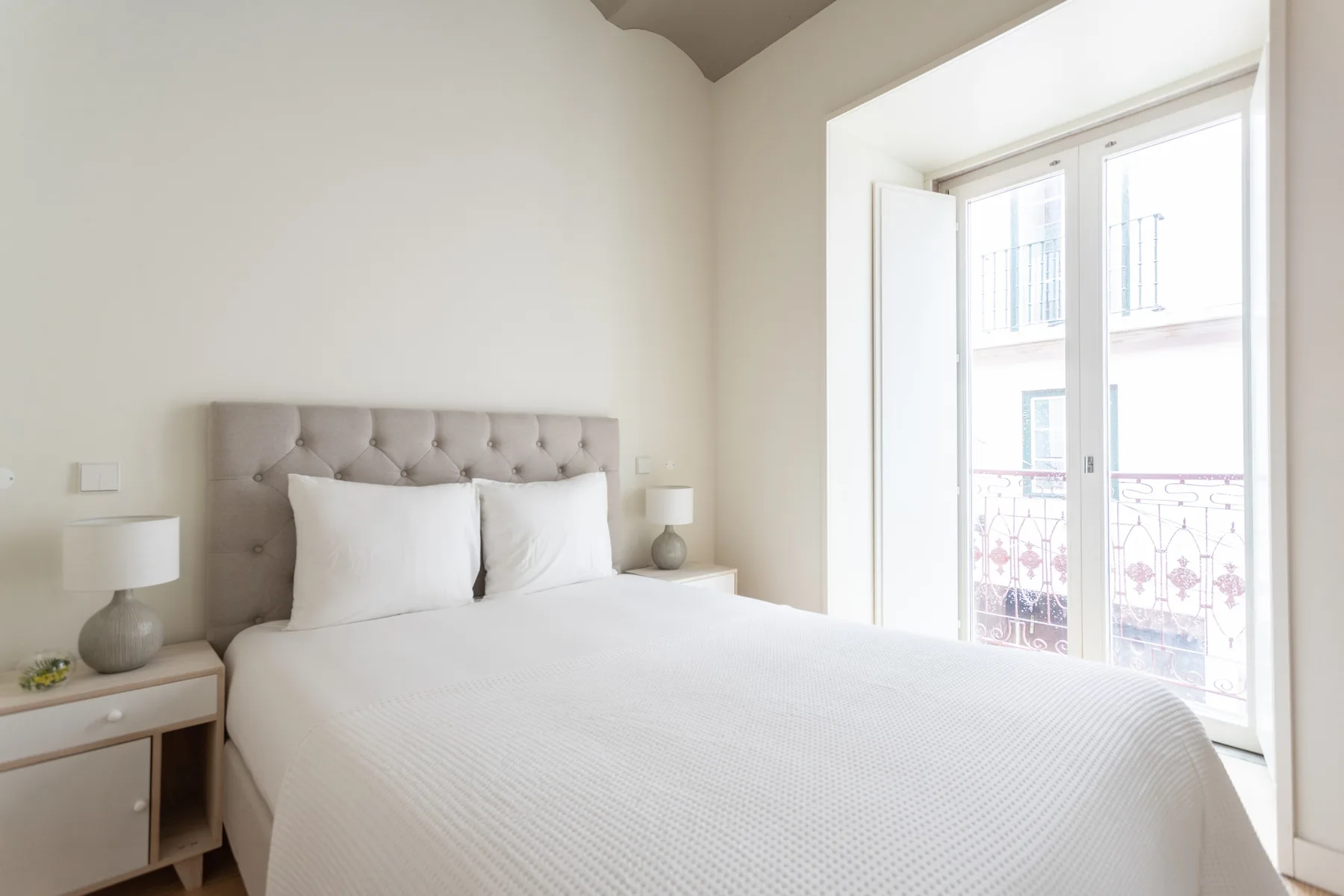 Un dormitorio luminoso con una cama junto a ventanas altas.
