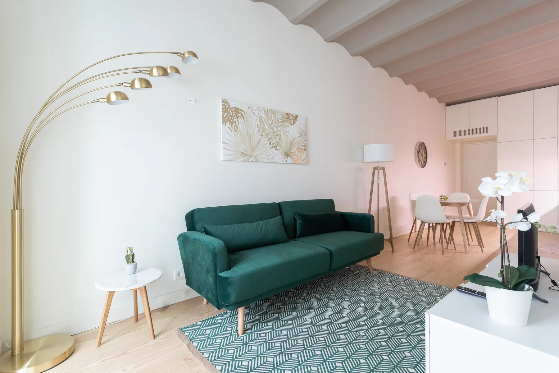 Zona de estar y comedor con asientos verdes, una alfombra y una mesa.