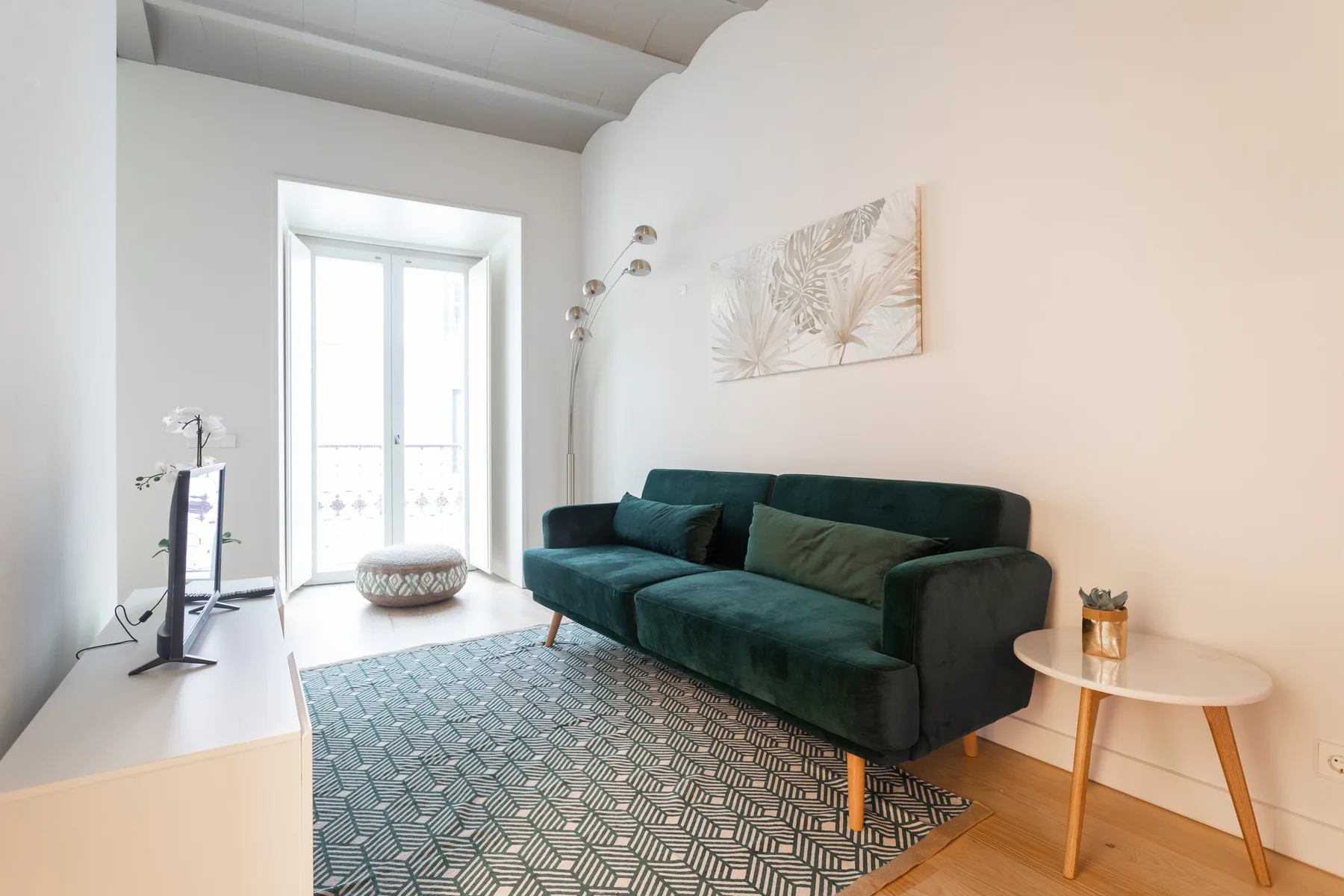 Una sala de estar luminosa con un sofá verde oscuro y una alfombra estampada.