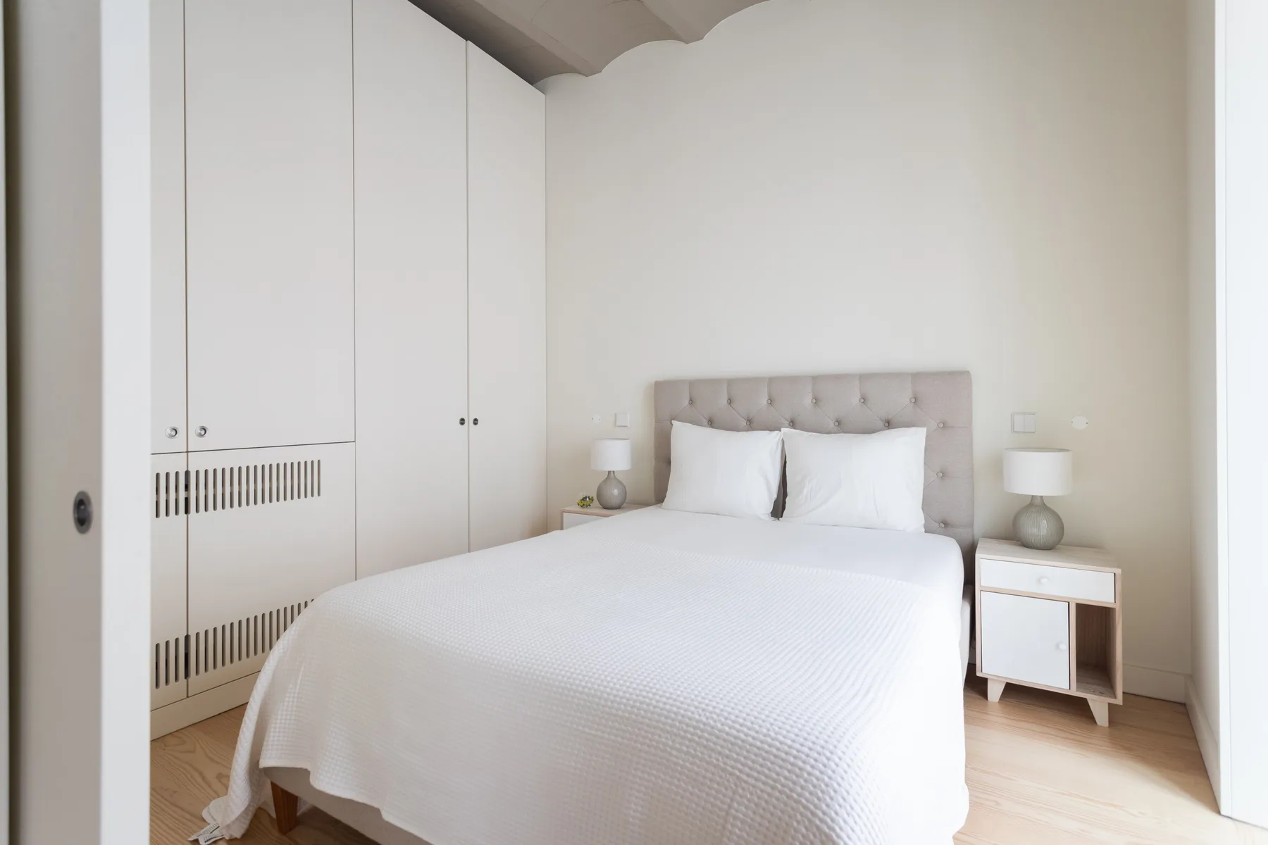 Un dormitorio luminoso con una cama, mesitas de noche y armarios empotrados.