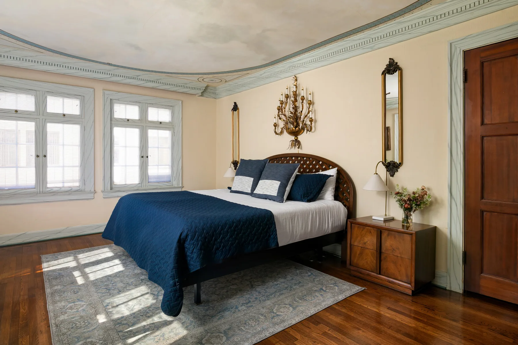 A bedroom with a bed dressed in blue and white linens beside two windows.